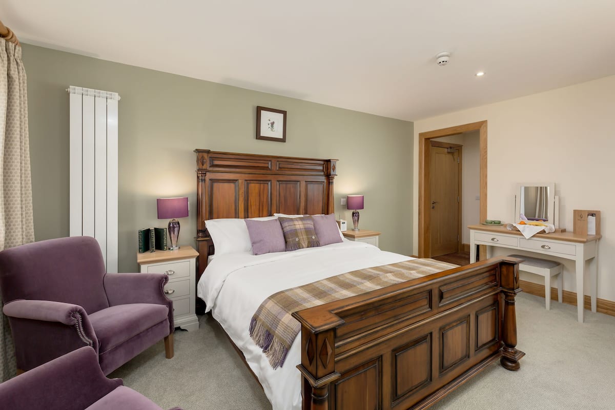A bedroom with a wooden bed, two bedside tables, a desk, and a chair.