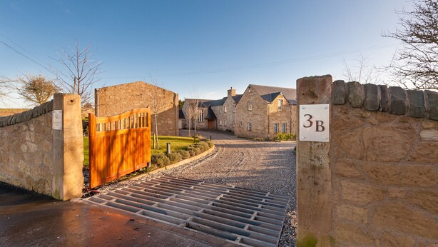 A stone-walled property with a wooden gate, a gravel driveway, and a sign indicating the property number 3B. - The Queens View Luxury B&B (Linlithgow)