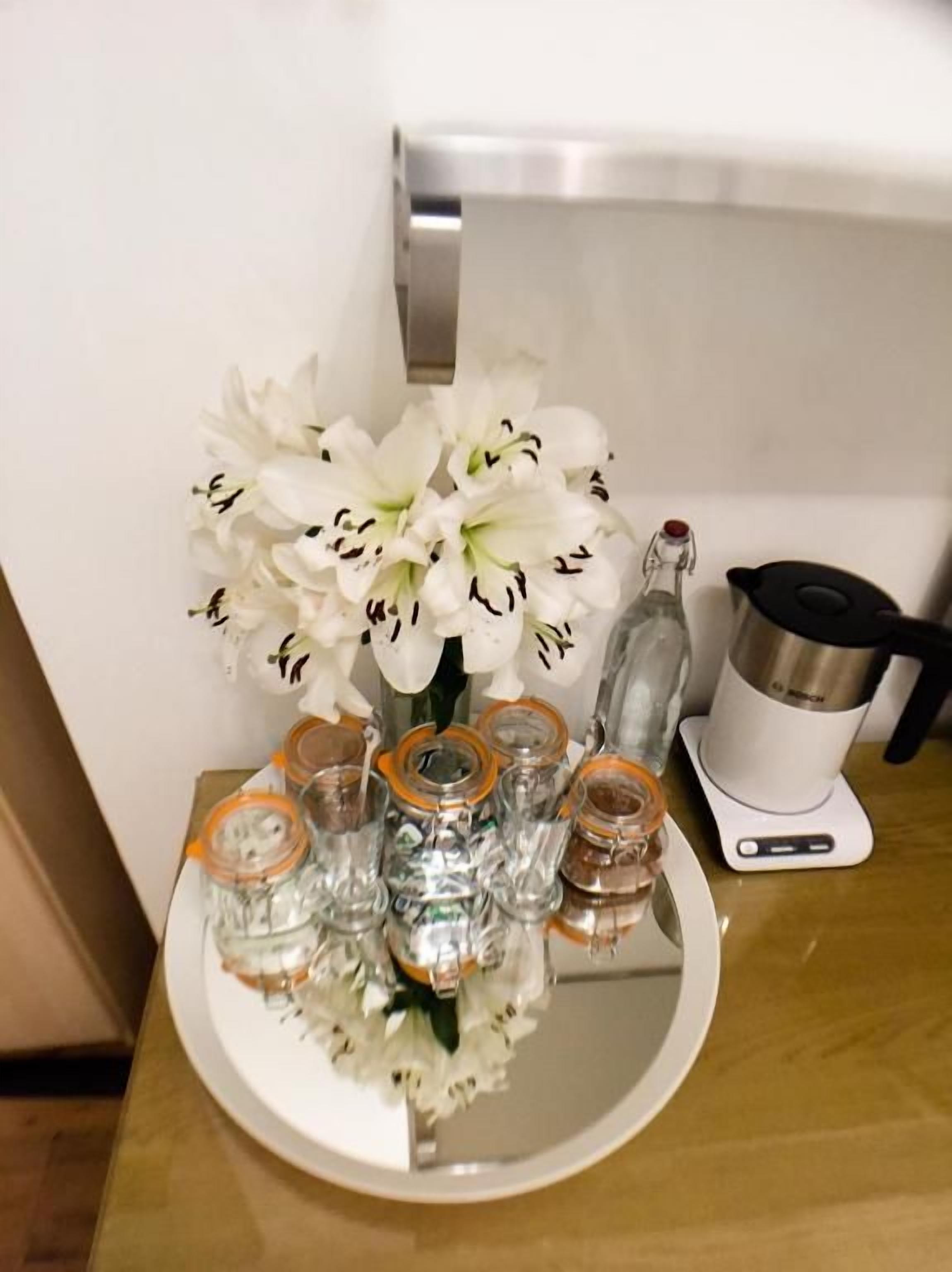 A kitchen counter with a white plate holding a bouquet of white flowers, a coffee maker, and several glass jars with orange lids.