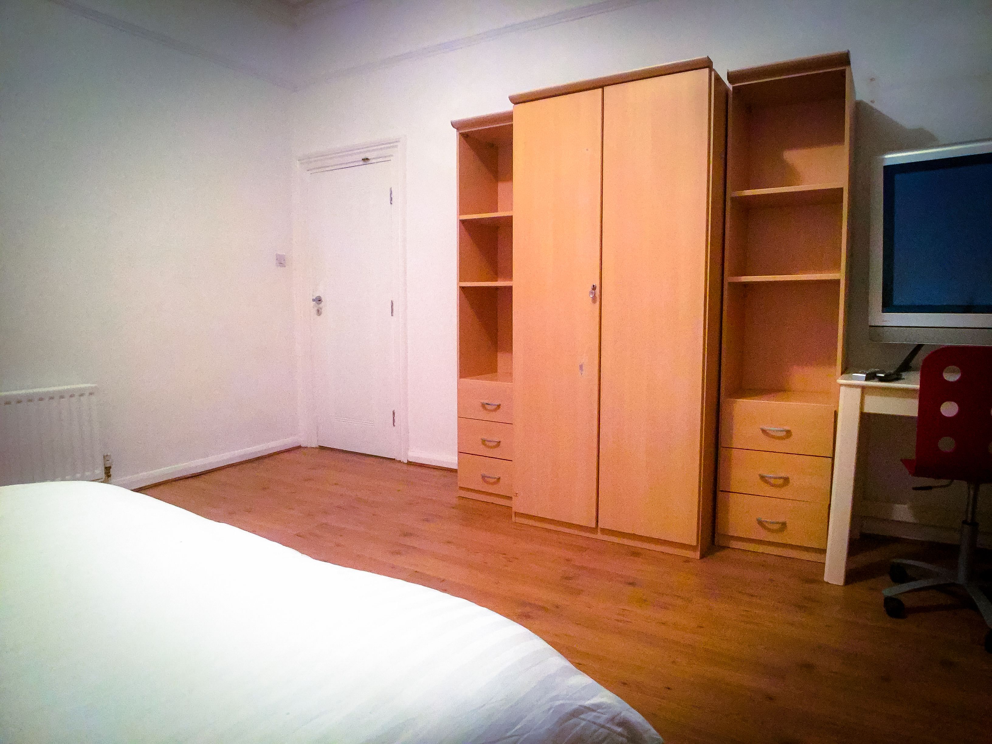 Une chambre à coucher avec un lit, une armoire en bois et un bureau avec un ordinateur.