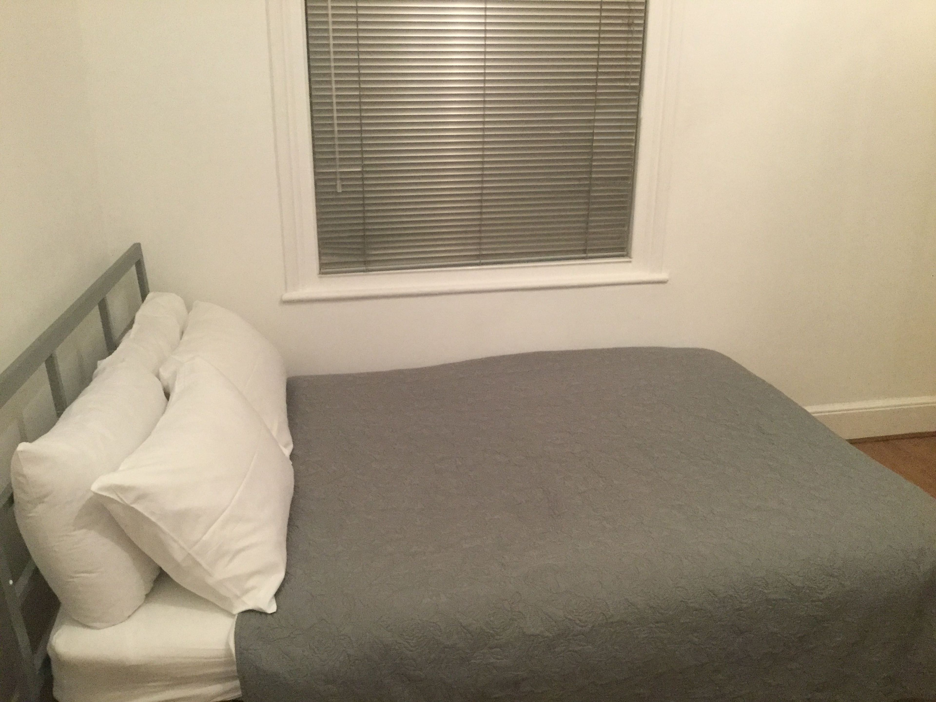 Un dormitorio con cama, almohadas y una ventana con persianas.