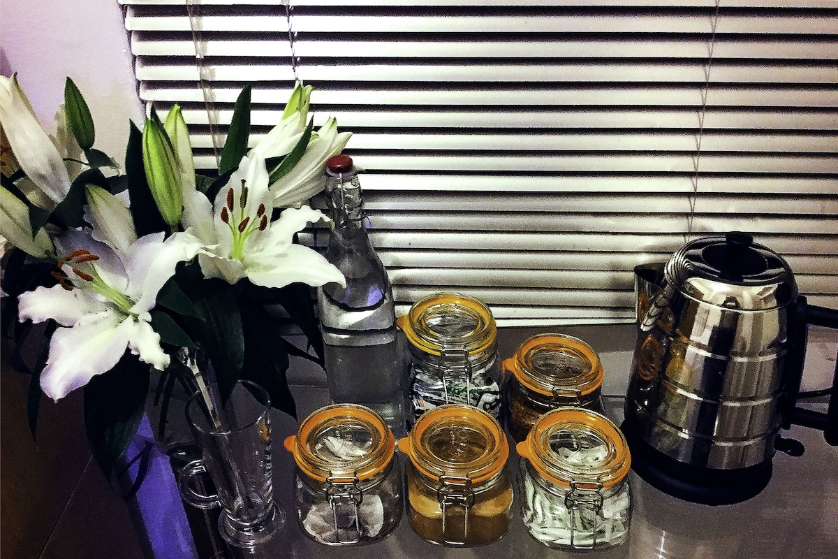 A kitchen counter with a flower vase, several glass jars with metal lids, and a stainless steel coffee pot.