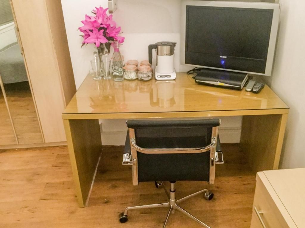 Um espaço de trabalho com escrivaninha de vidro, cadeira de escritório preta, monitor de computador e máquina de café.