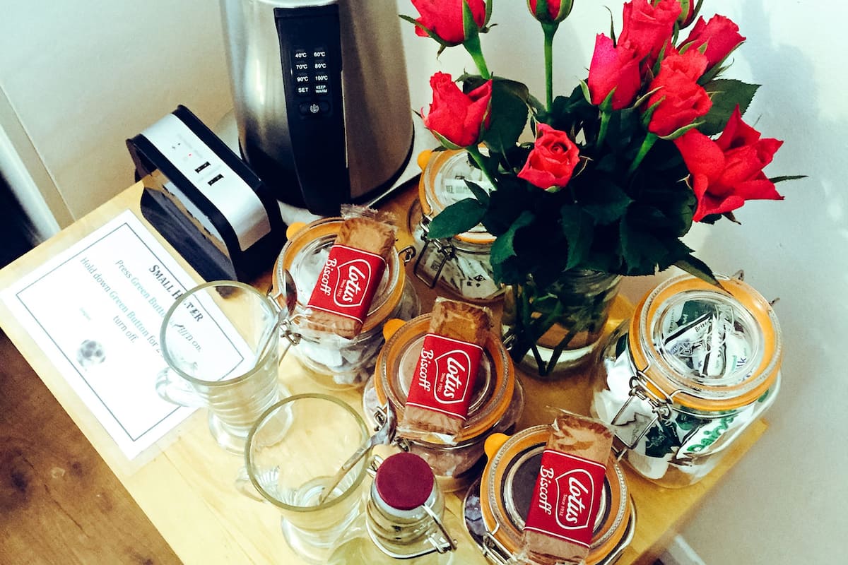 A wooden table with a coffee maker, red roses, and jars of biscuits.