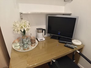 A hotel room desk with a flat-screen TV, a coffee maker, a remote control, and a tray with glassware and a vase of flowers. - Outram 26 (Stockton-on-Tees)