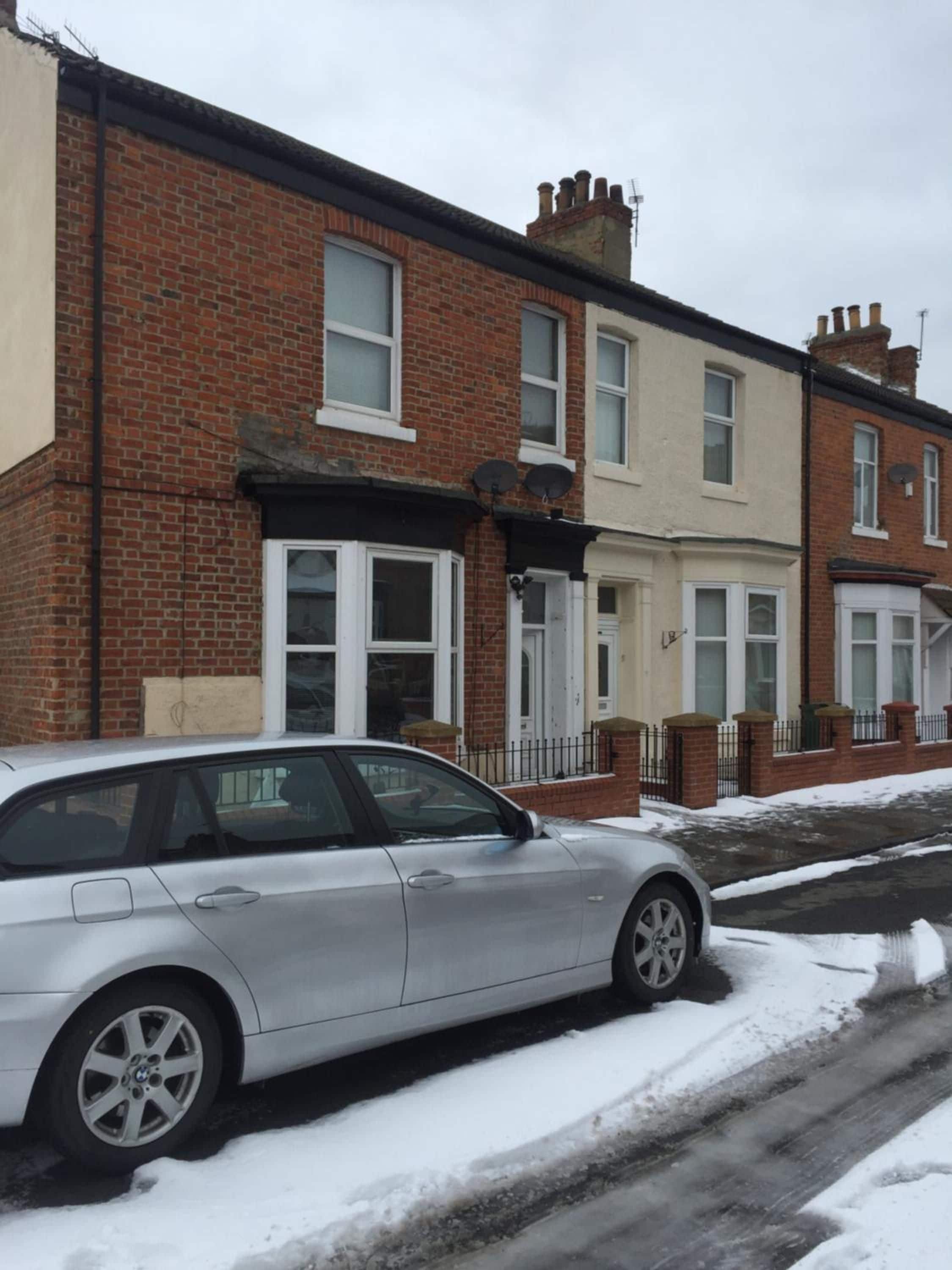 A residential street with houses, a parked car, and snow on the ground.