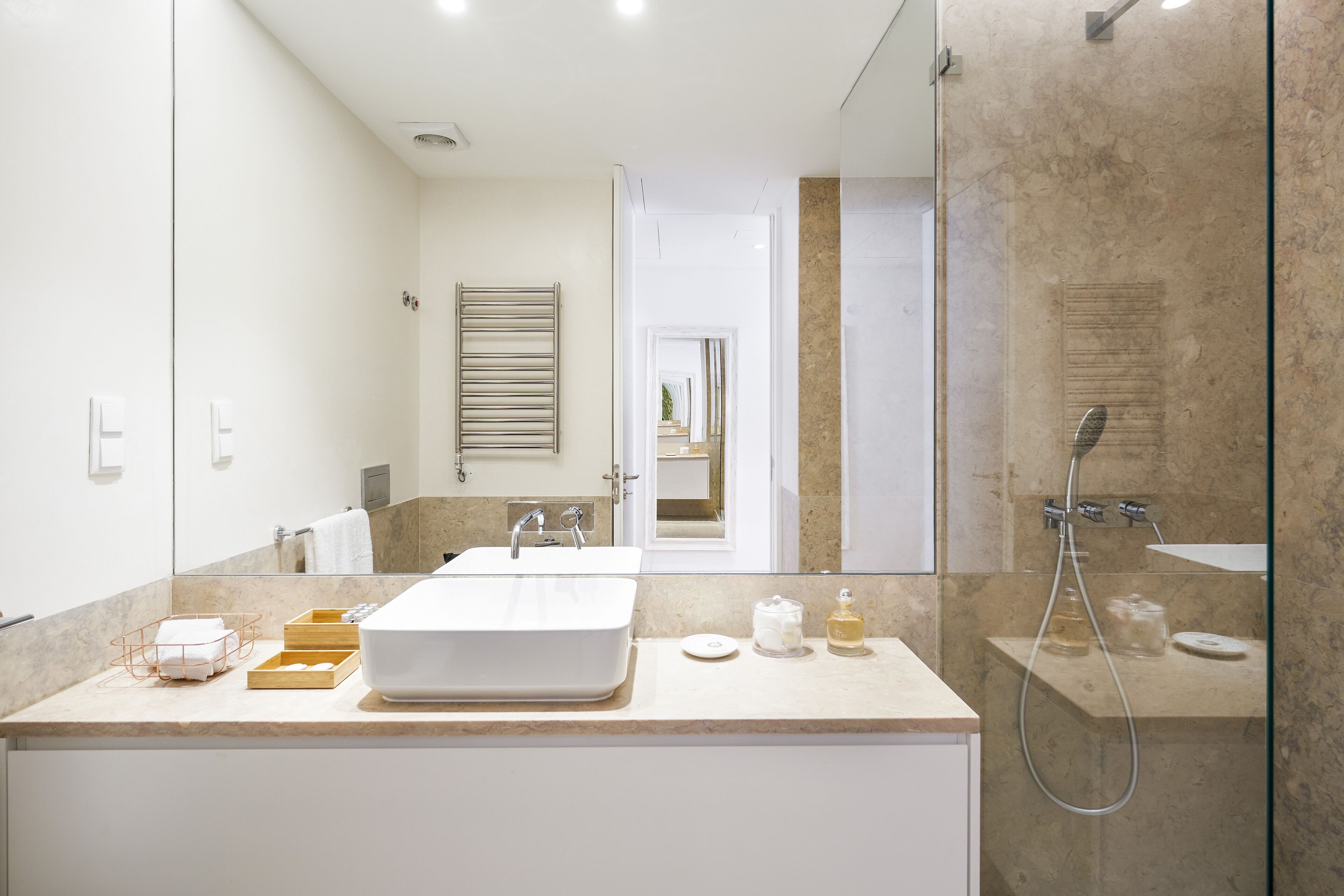 Een moderne badkamer met een grote spiegel, twee wastafels, een douche en een marmeren aanrechtblad.
