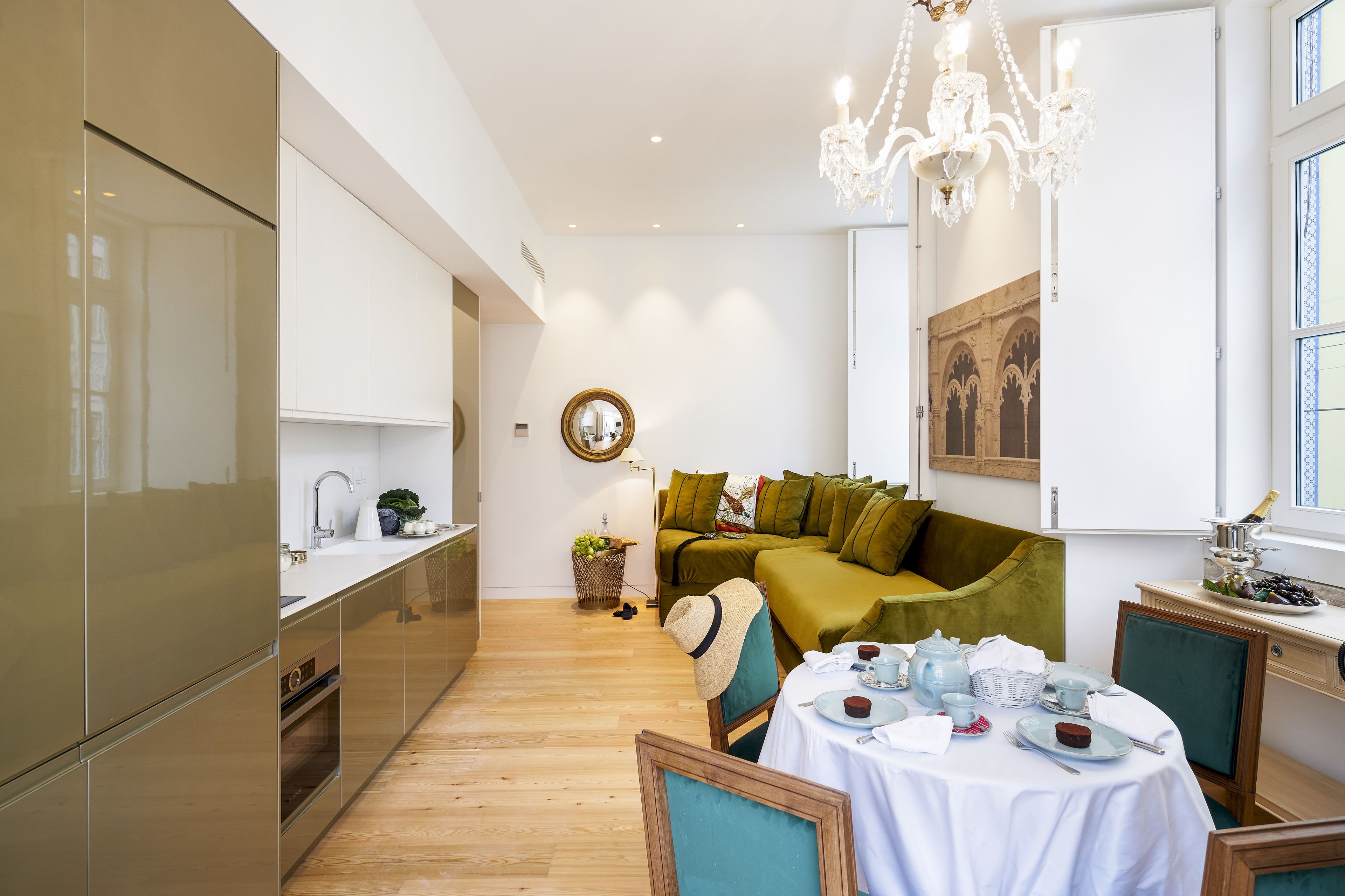 A modern kitchen with a dining area, a chandelier, and a green sofa.