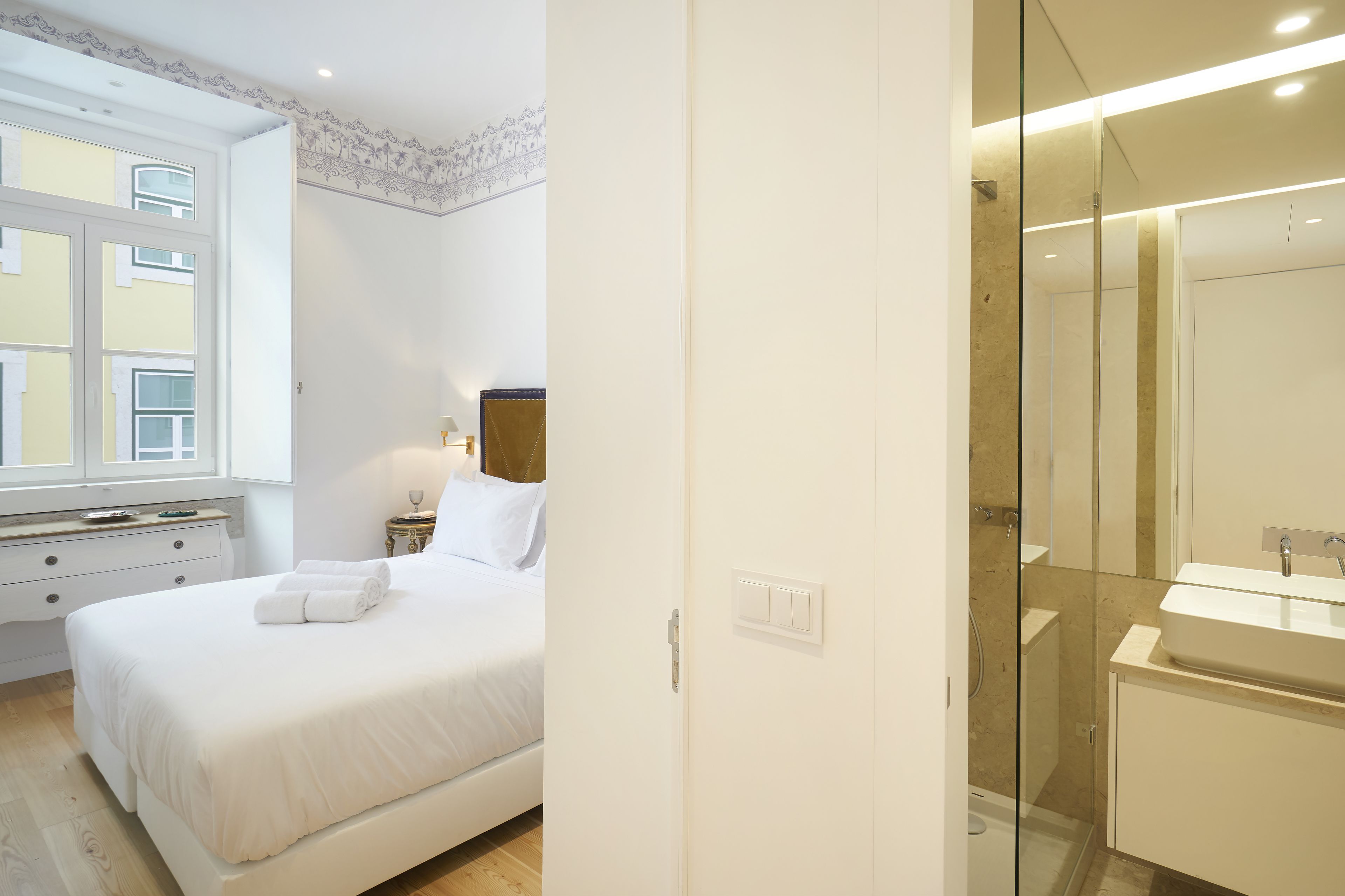 Un dormitorio con cama, mesita de noche, lámpara y ventana.