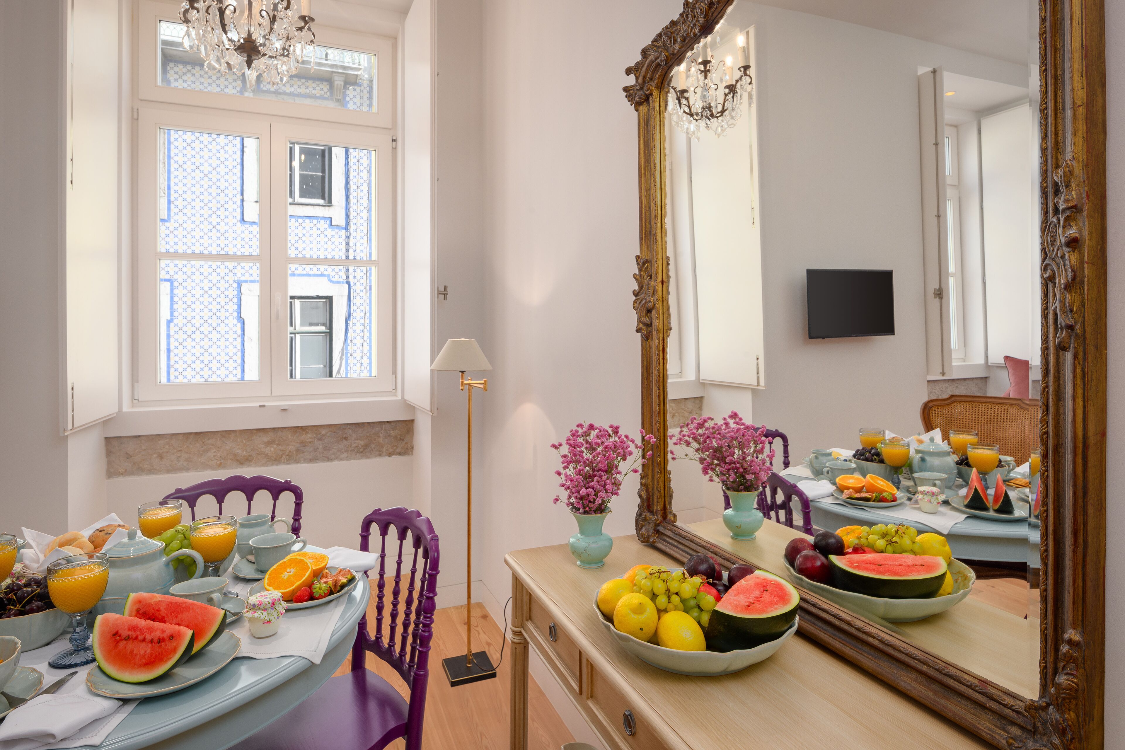 A breakfast table with fruit, a mirror, and a window with patterned curtains.