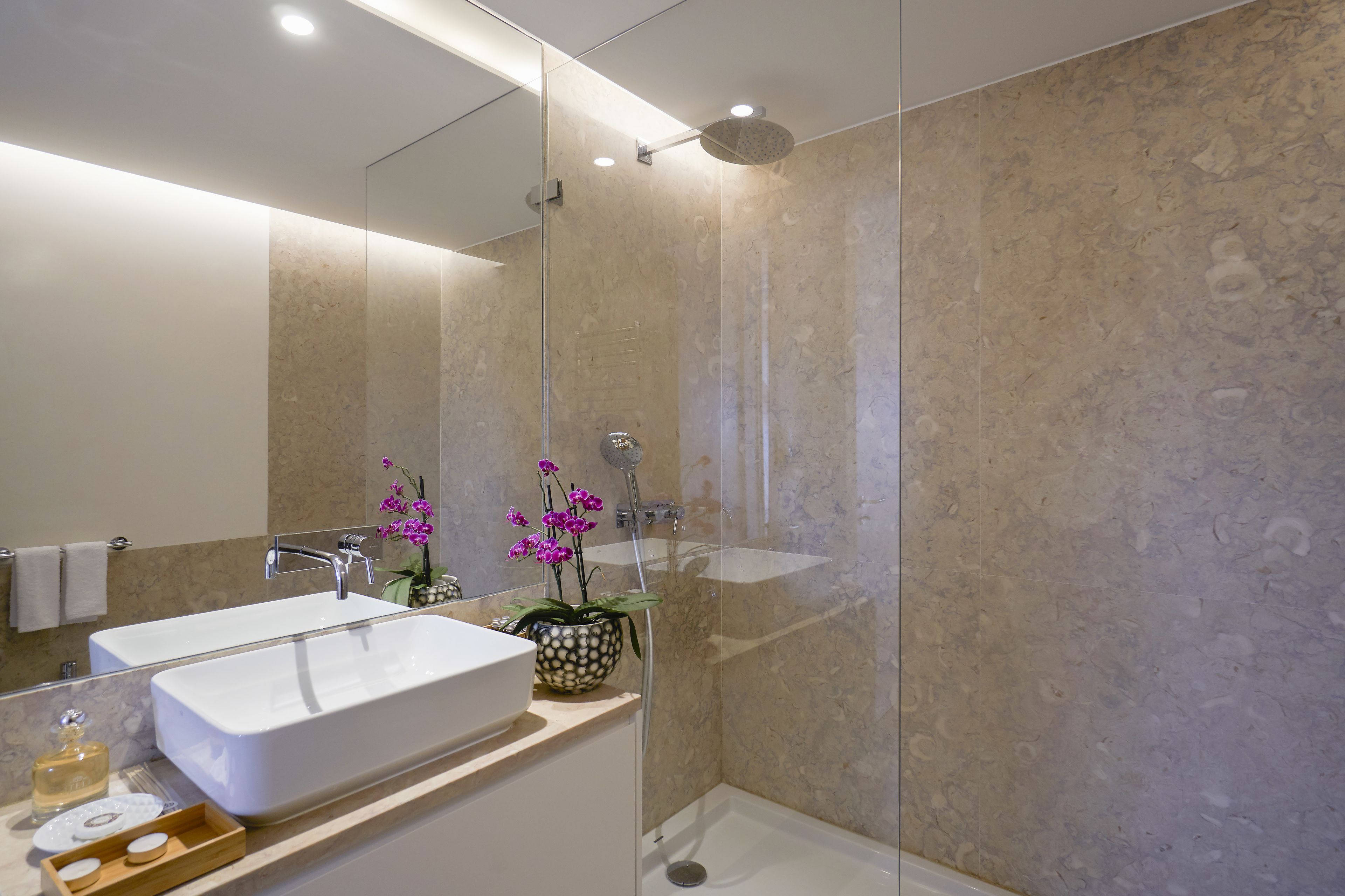A modern bathroom with a large rectangular sink, a glass-enclosed shower, and a potted orchid plant.