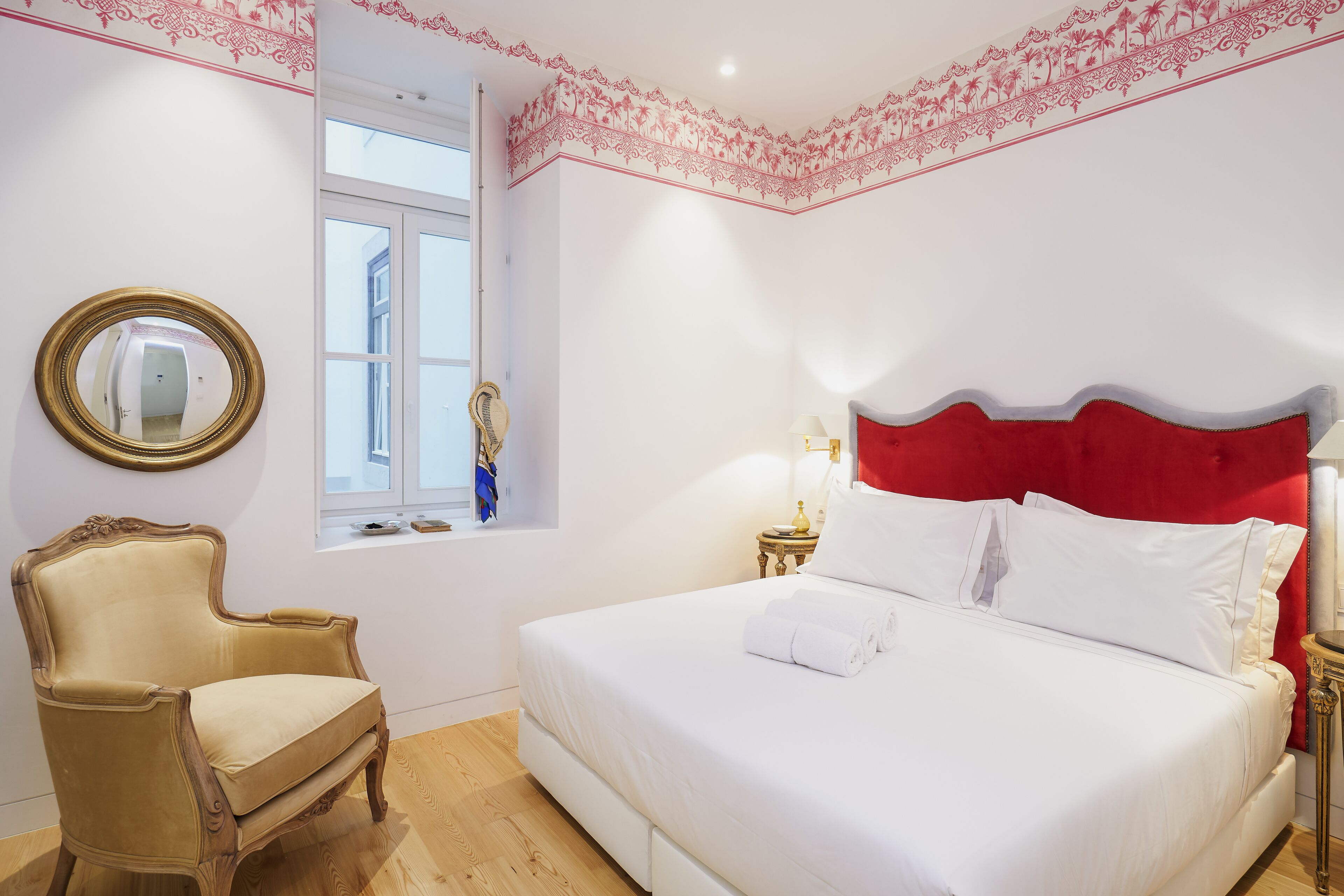 Een slaapkamer met een bed, een stoel, een raam en een spiegel.