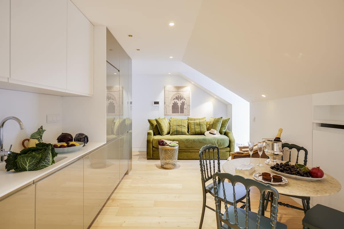 A modern kitchen with a dining area, a green sofa, and a table set with food and drinks.