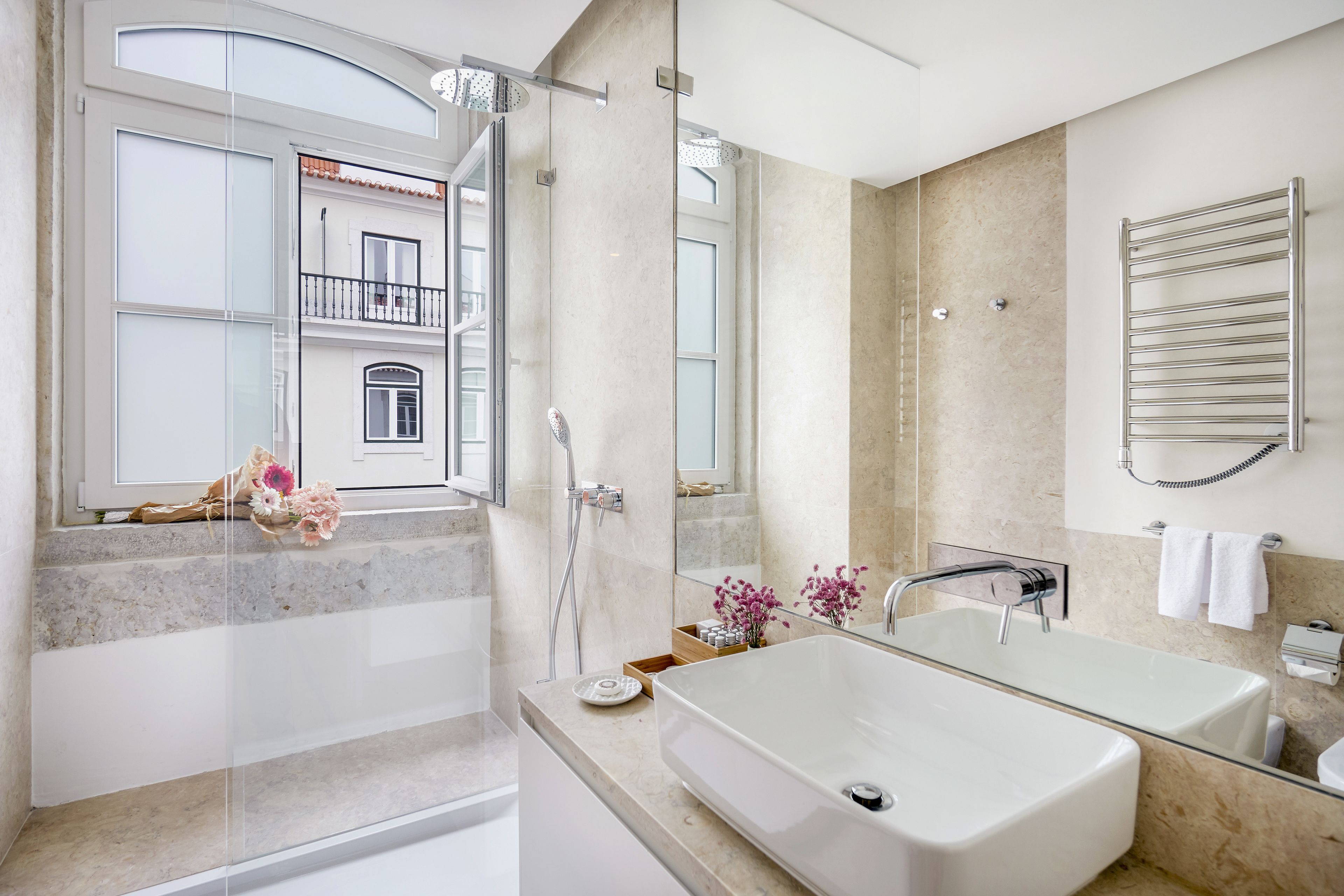 A modern bathroom with a large bathtub, a glass shower enclosure, and a view of a building with balconies.