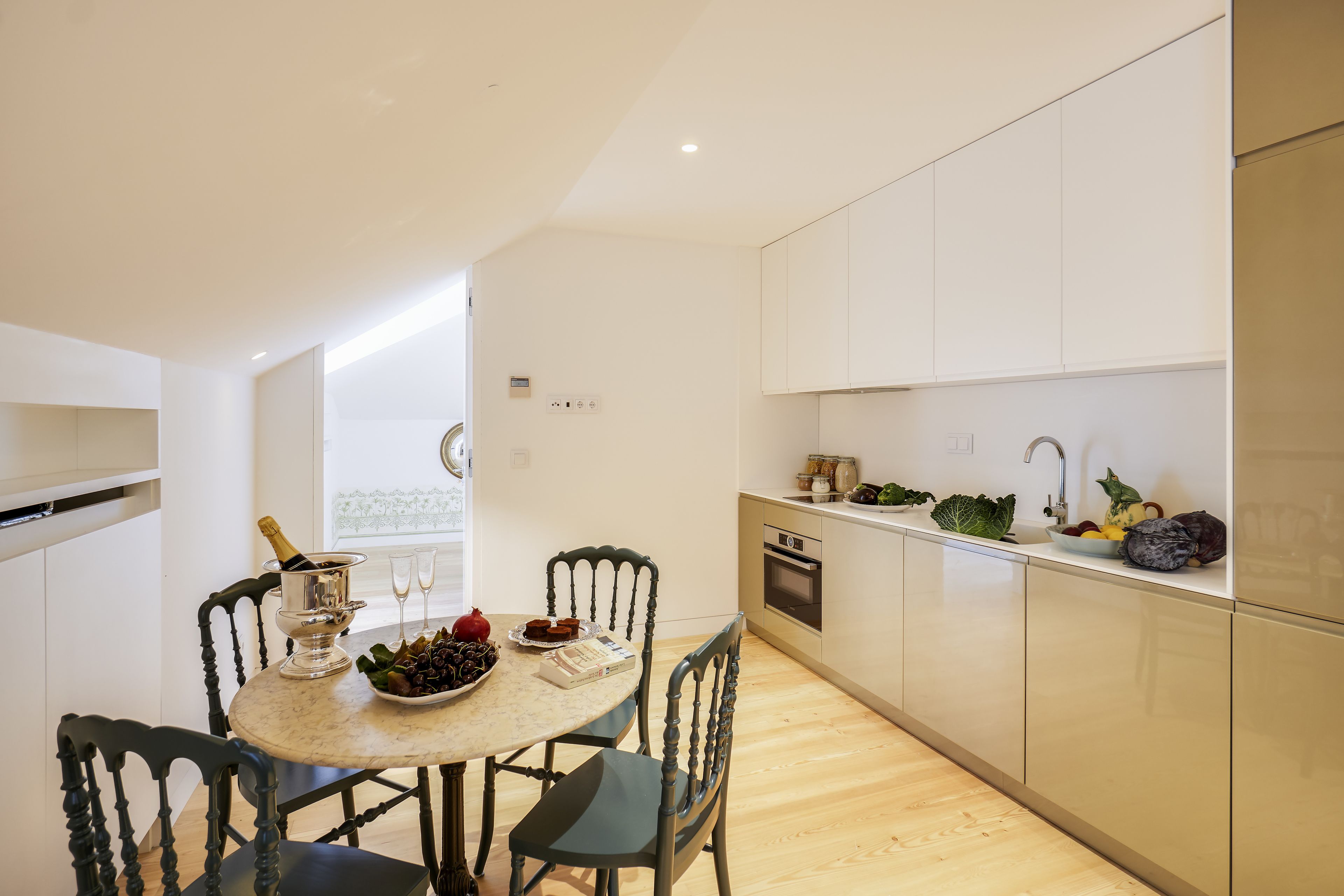 A modern kitchen with a dining table set for two, a built-in oven, and a variety of fresh produce on the counter.