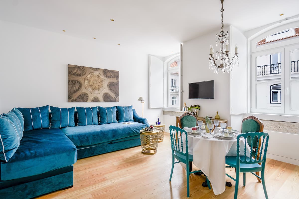 A modern living room with a blue sofa, a dining table with chairs, and a chandelier.