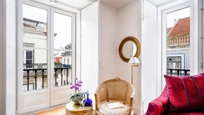 A cozy living room with a wicker chair, a red sofa, and a small round table with a vase and flowers. - Residentas Aurea (Lisbon)