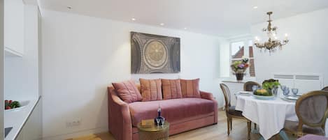 A modern living room with a pink sofa, a round coffee table, and a dining area with a white tablecloth.