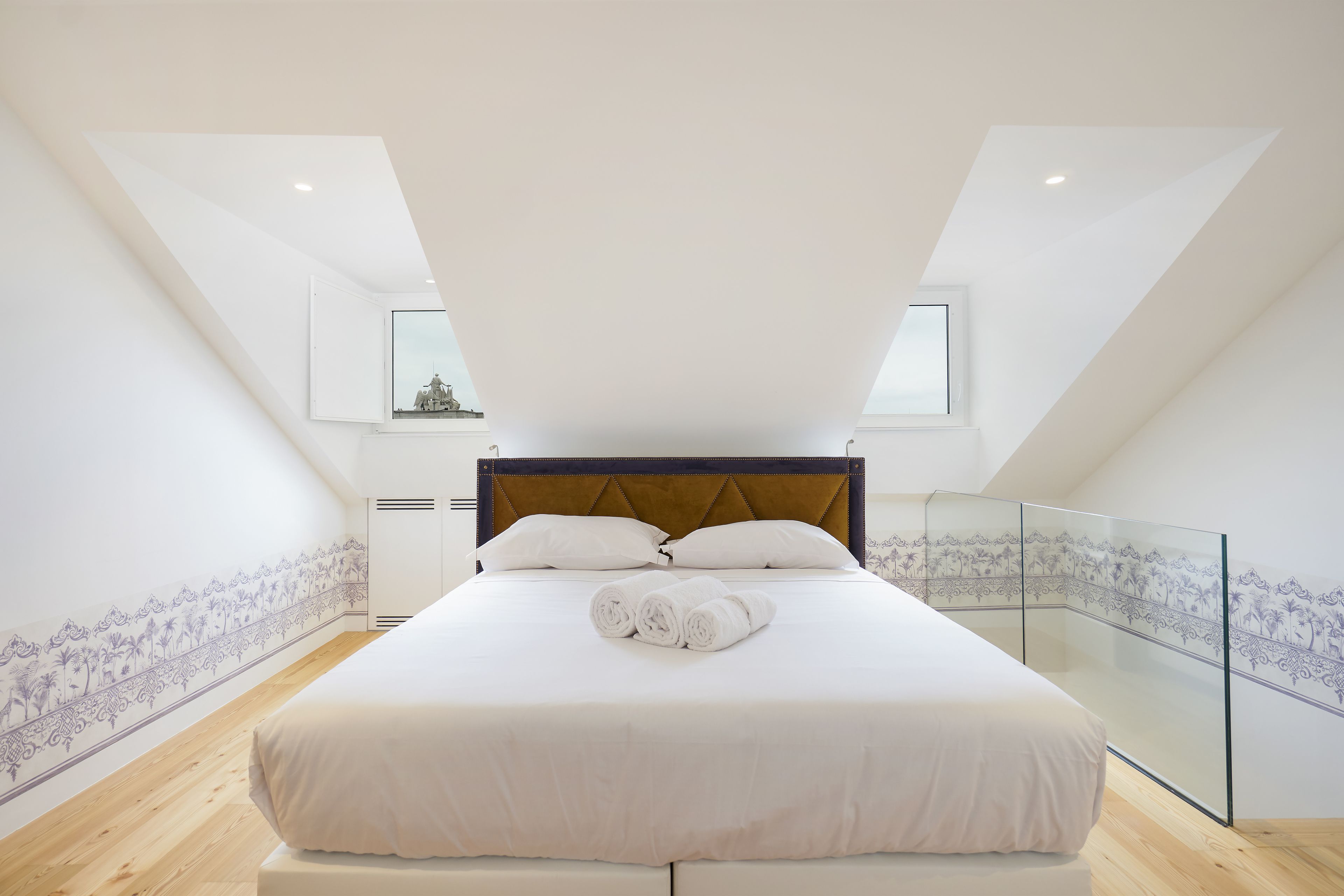A modern bedroom with a large bed, a wooden floor, and a glass partition.
