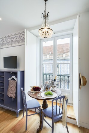 Spiseområde med et rundt bord, stole, en lysekrone og udsigt til en balkon med et tegltag.