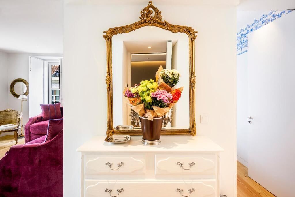 Una habitación con un aparador blanco, un espejo grande y ornamentado, y un florero con flores.