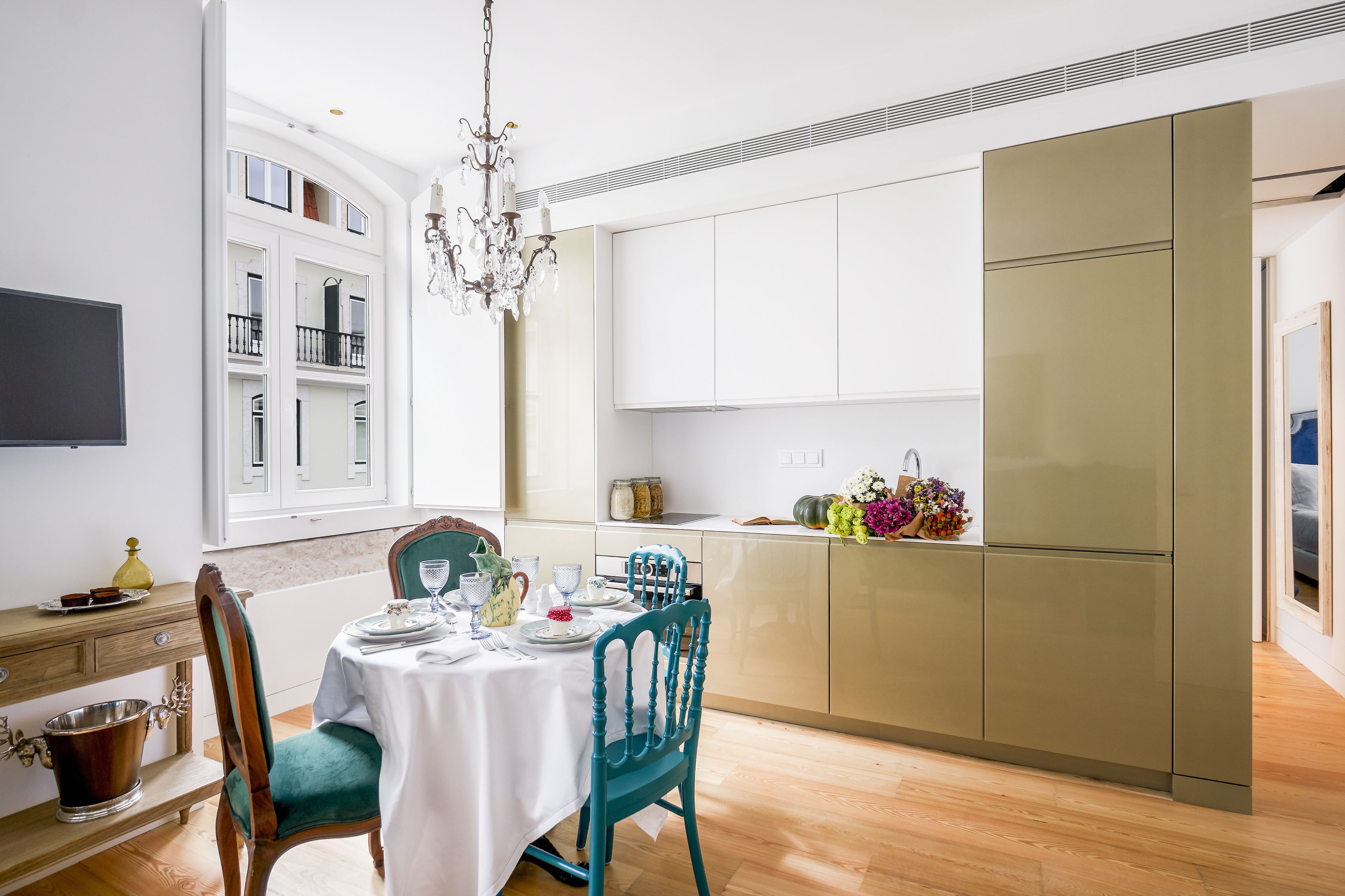 A modern dining area with a table set for four, a chandelier, and a kitchen with a large refrigerator.
