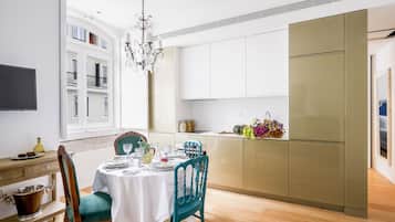 A modern dining area with a table set for four, a chandelier, and a kitchen with a large refrigerator.