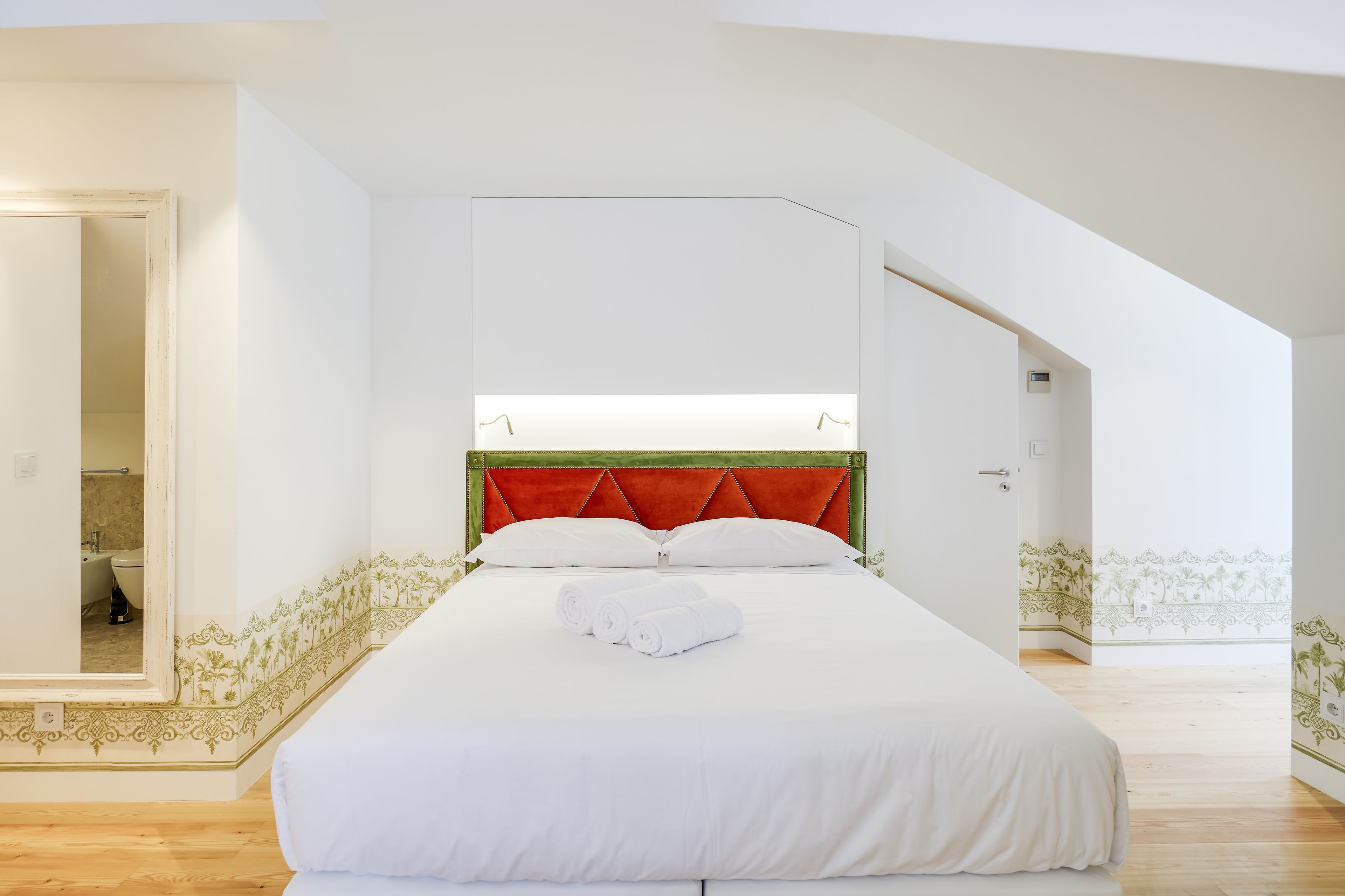Ein Schlafzimmer mit einem großen Bett, einem roten Kopfteil und Blick ins Badezimmer durch eine offene Tür.