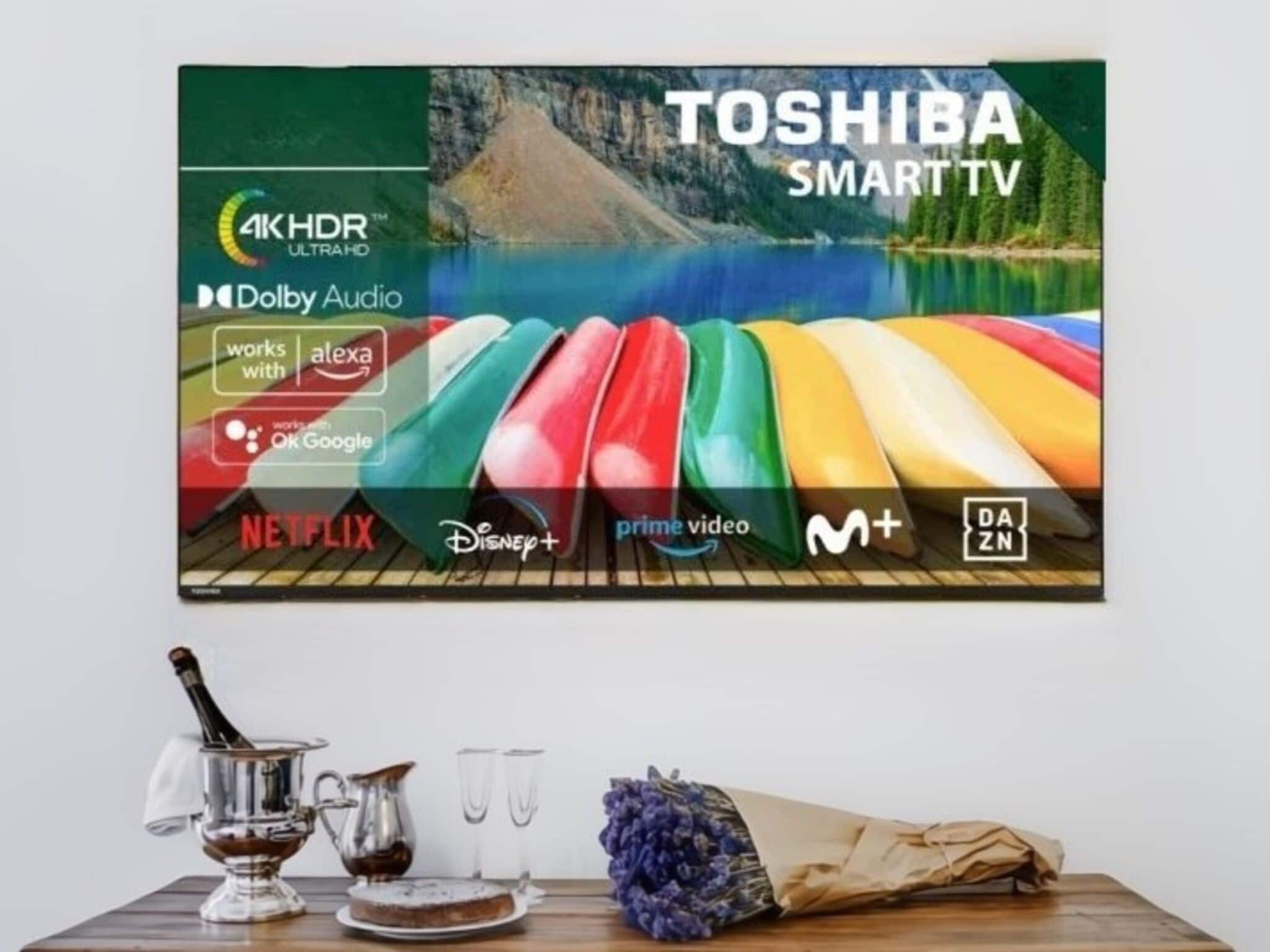 A wall-mounted TV with a Toshiba SmartTV logo, 4K HDR, Dolby Audio, and logos for Netflix, Disney+, Prime Video, M+, DAZN, and Alexa compatibility.