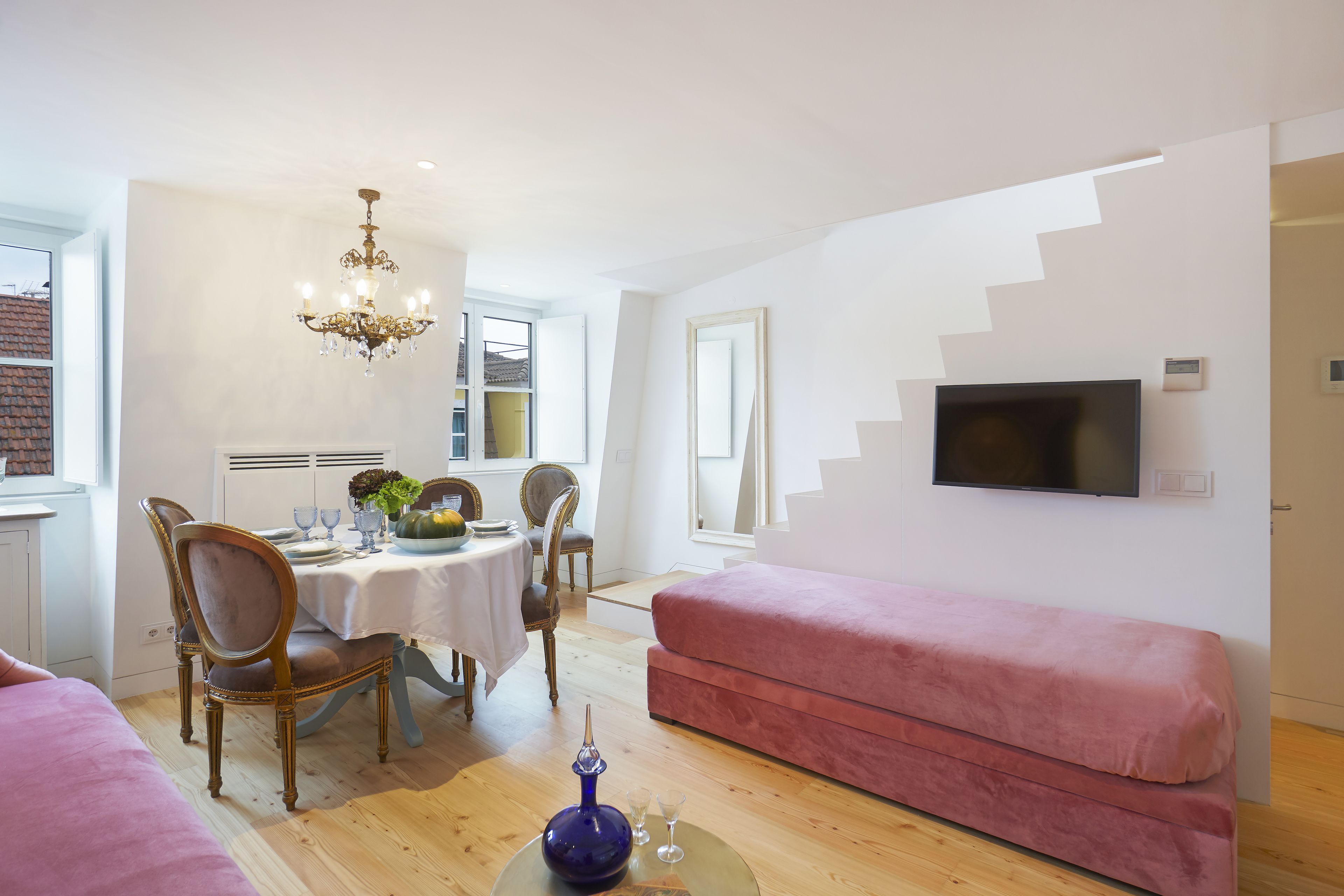 Un salon avec un canapé rose, un coin repas avec une table dressée pour quatre personnes et un téléviseur fixé au mur.