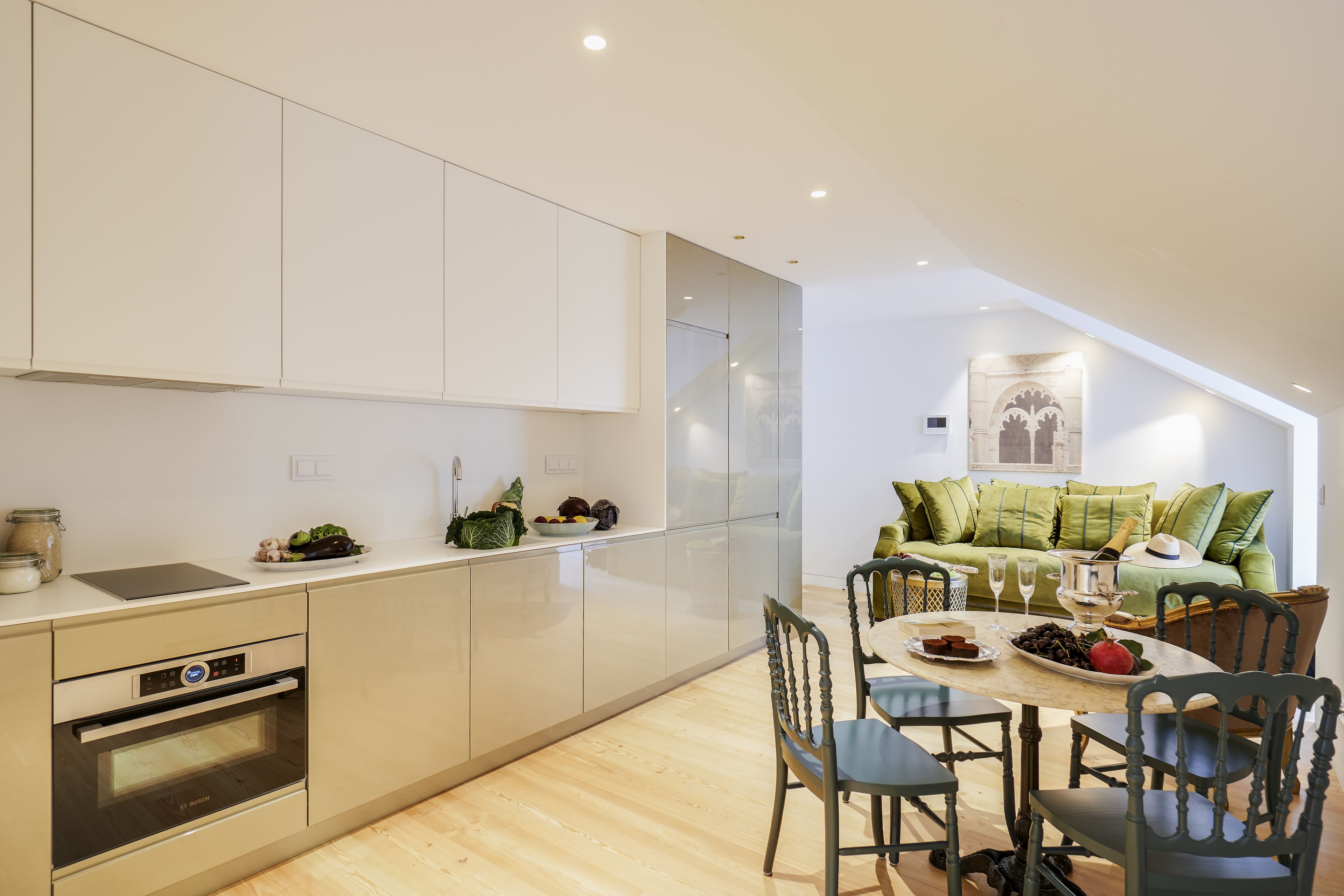 Cozinha moderna com eletrodomésticos integrados, área de refeições com piso de madeira e sofá estofado verde na sala de estar.