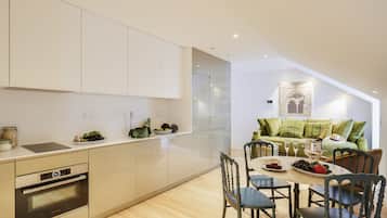 Cozinha moderna com eletrodomésticos integrados, área de refeições com piso de madeira e sofá estofado verde na sala de estar.