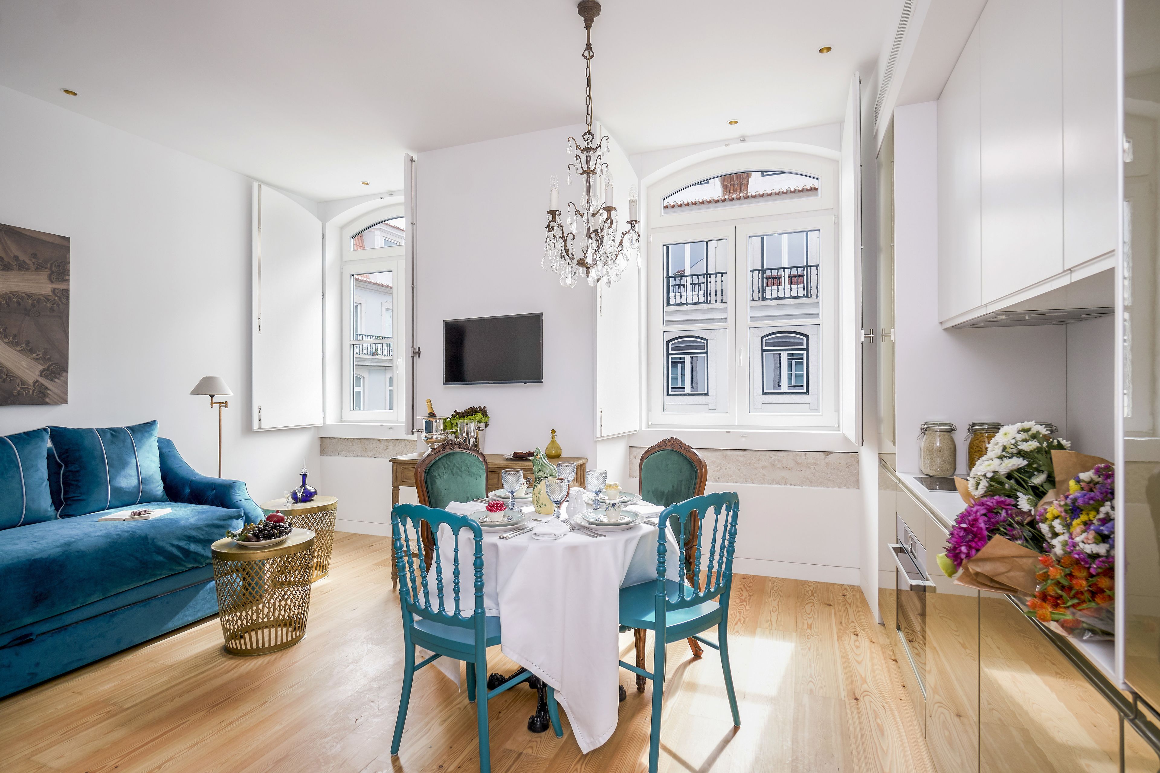 A modern living room with a blue sofa, teal chairs, a dining table set for four, and a chandelier.