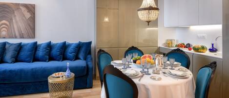 A modern dining area with a round table set for six, blue upholstered chairs, a blue sofa, and a chandelier.