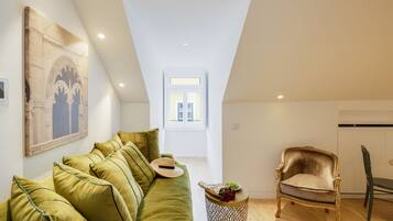 Un dormitorio tipo loft moderno con techo alto, un sofá de terciopelo verde, un sillón antiguo y un ventanal que proporciona luz natural.