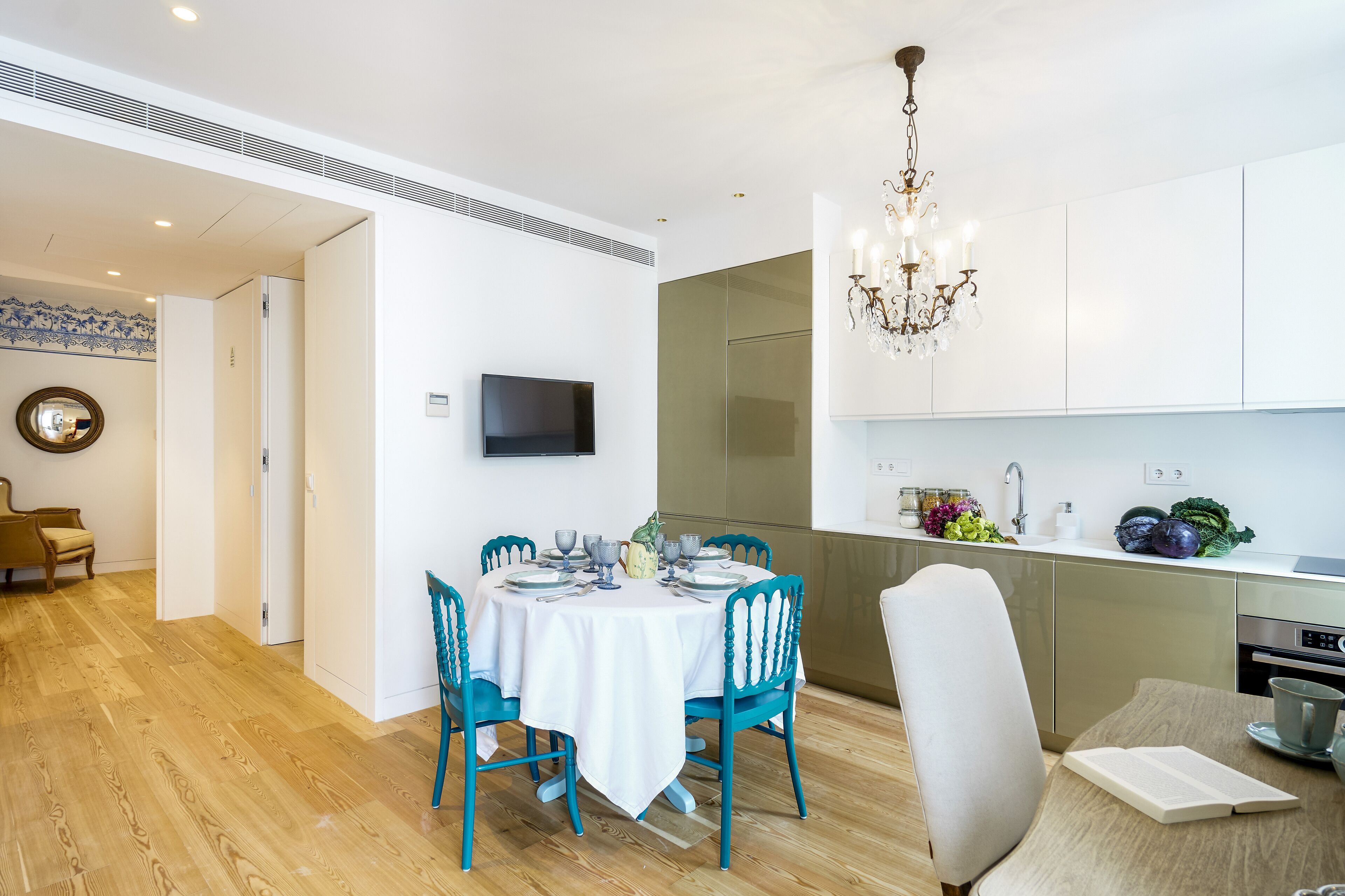 Una cocina moderna con comedor, que incluye una araña, un televisor de pantalla plana y una mesa de madera con sillas.