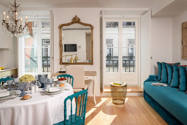 Un comedor con una mesa redonda dispuesta para una comida, un sofá azul aguamarina y un espejo grande.