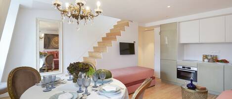 A dining area with a chandelier, a staircase, a kitchen, and a mirrored wall.