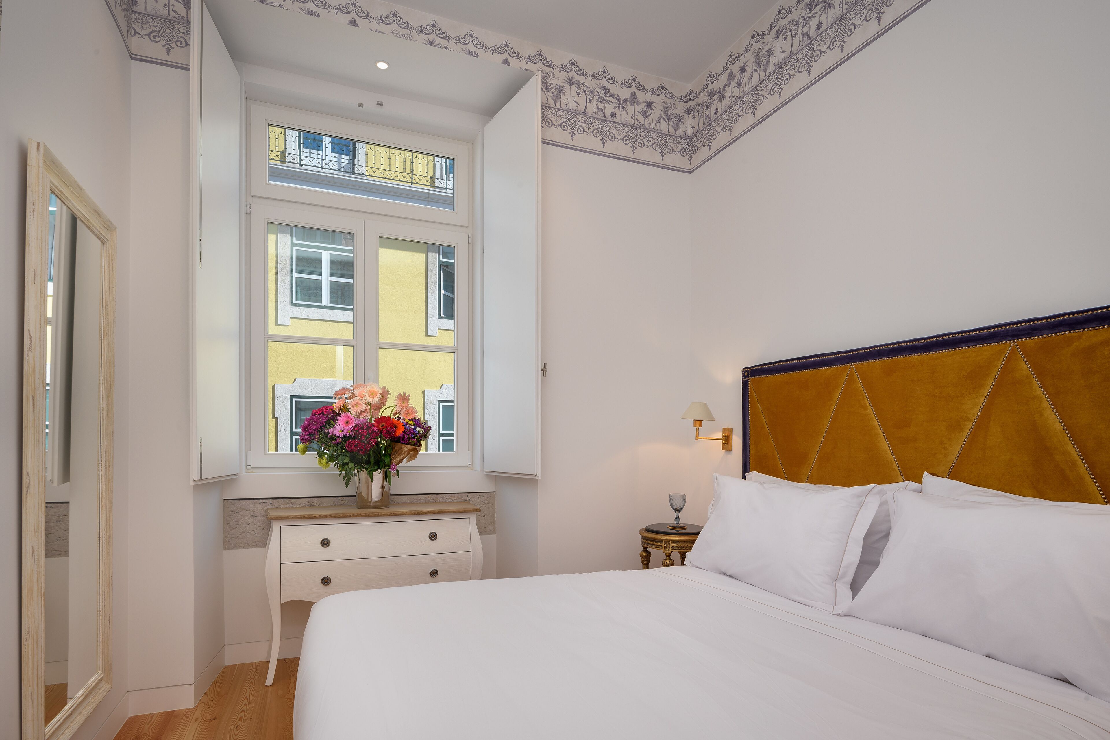 Un dormitorio con cama, mesita de noche, cómoda, ventana con vistas y techo decorativo.