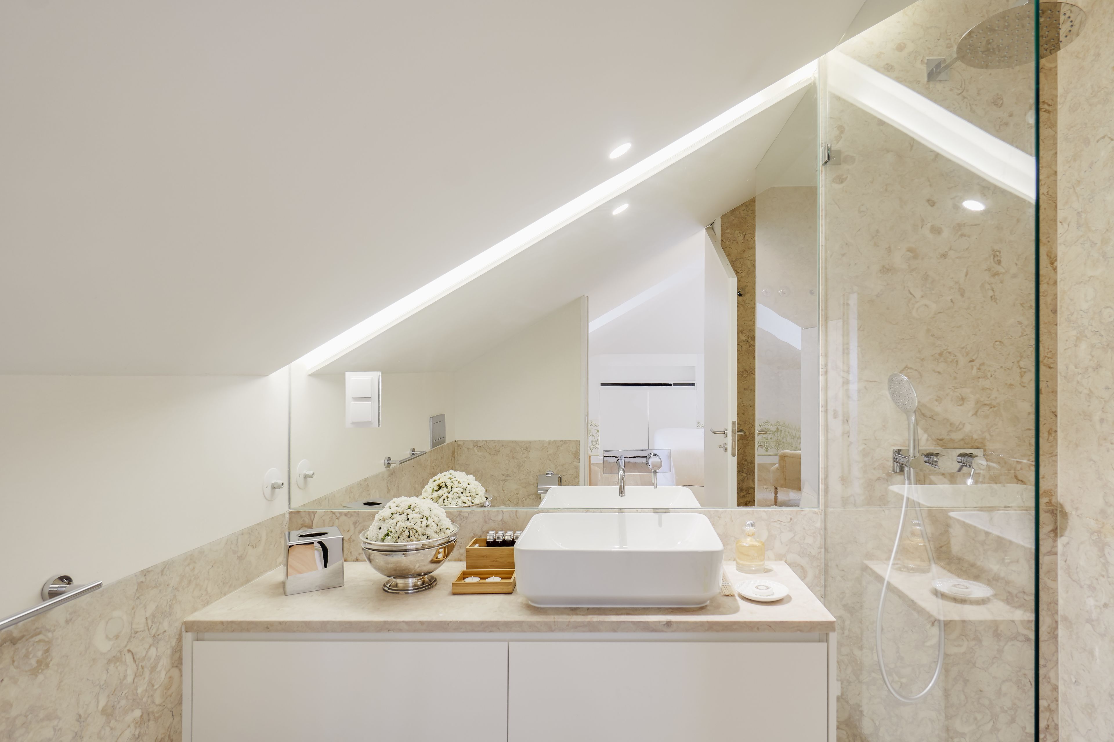 A modern bathroom with a large mirror, a white sink, a glass shower enclosure, and marble countertops.