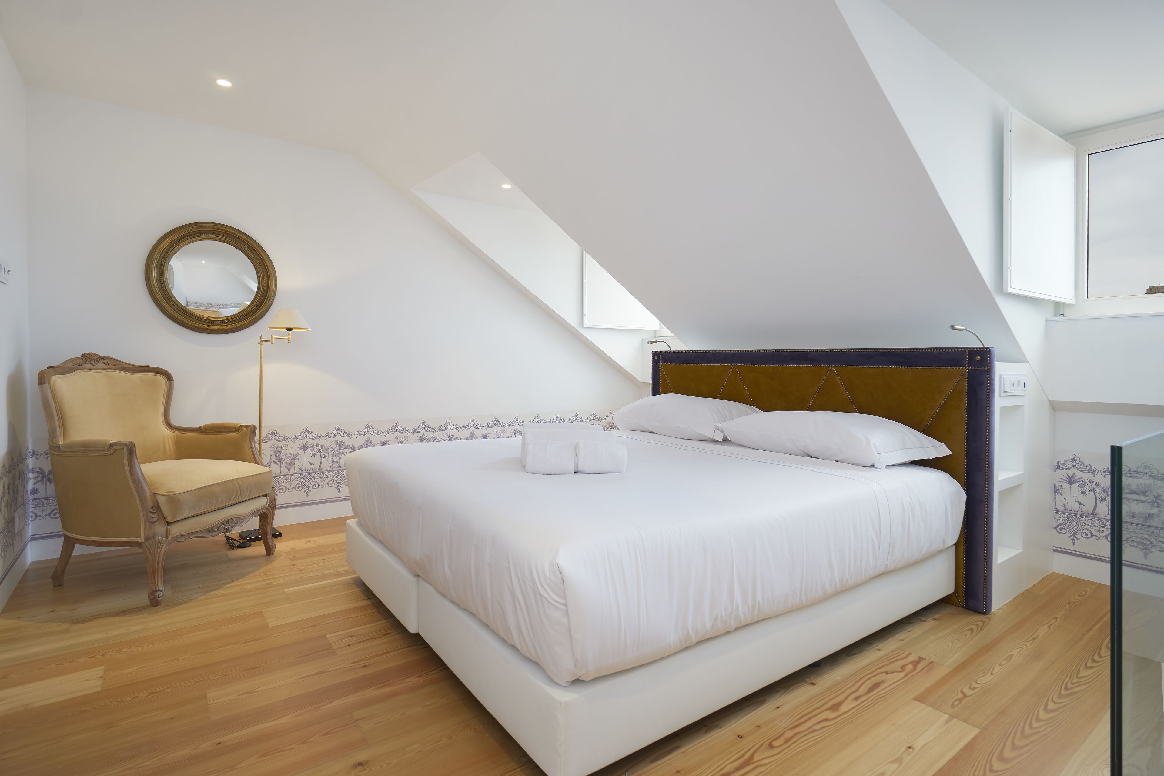 Un dormitorio con una cama grande, una silla, una lámpara de pie y un espejo en la pared.