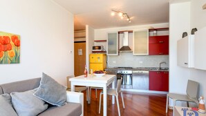 A modern kitchen with red cabinets, a white countertop, and a dining area with a white table and chairs. - Desenzanoloft – Butterfly and Pools (Desenzano del Garda)