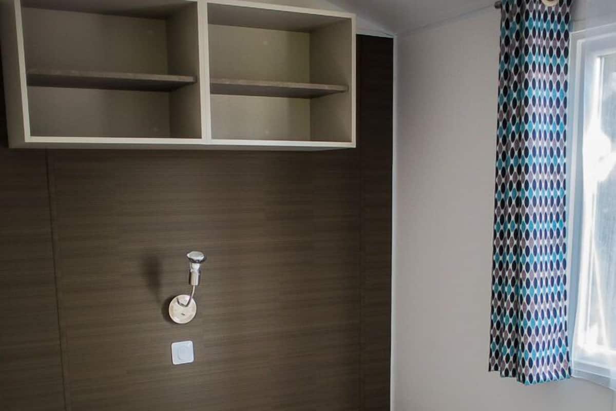 A compact room with two single beds, a small bedside table, a wall-mounted light, and a window with patterned curtains.