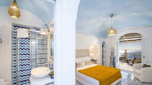 A modern bathroom with a shower, sink, and vanity. The bedroom features a large bed, a view of the sea, and a balcony with outdoor furniture. - B&B La Barbera (Praiano)