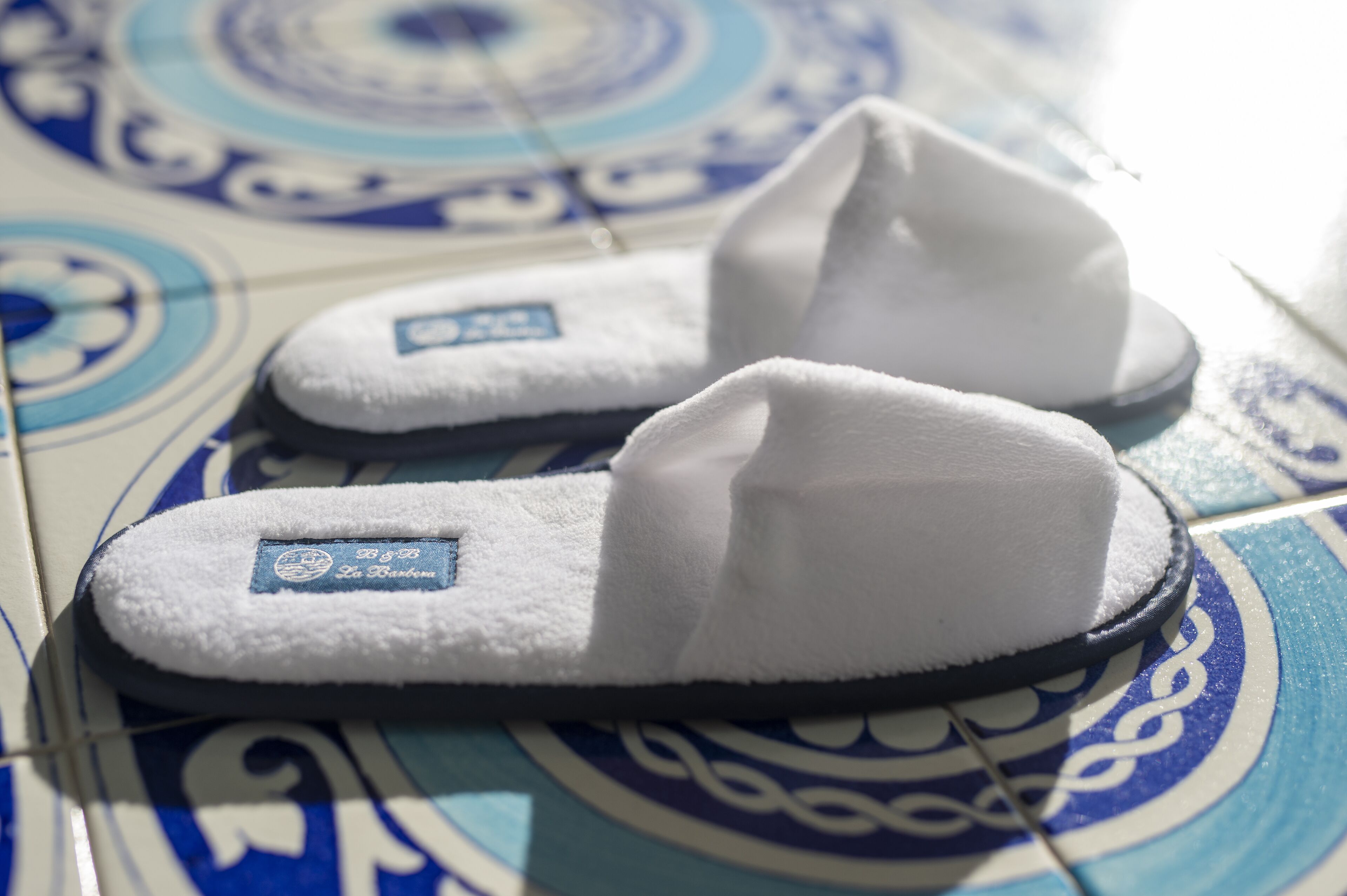 A pair of white slippers with a label on a tiled floor with a blue and white pattern.