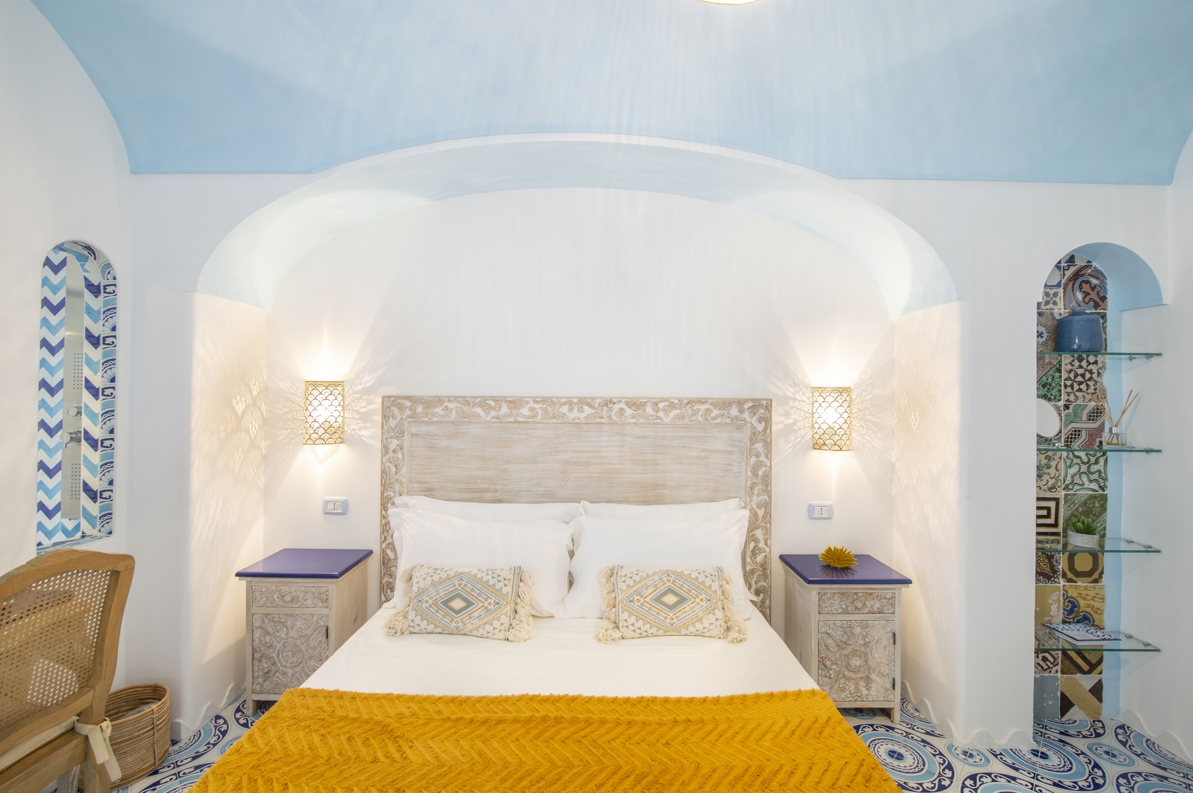 A bedroom with a bed, two nightstands, a chair, and a decorative shelf.