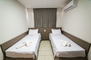 A hotel room with two single beds, a large window with curtains, an air conditioning unit, and a tiled floor.
