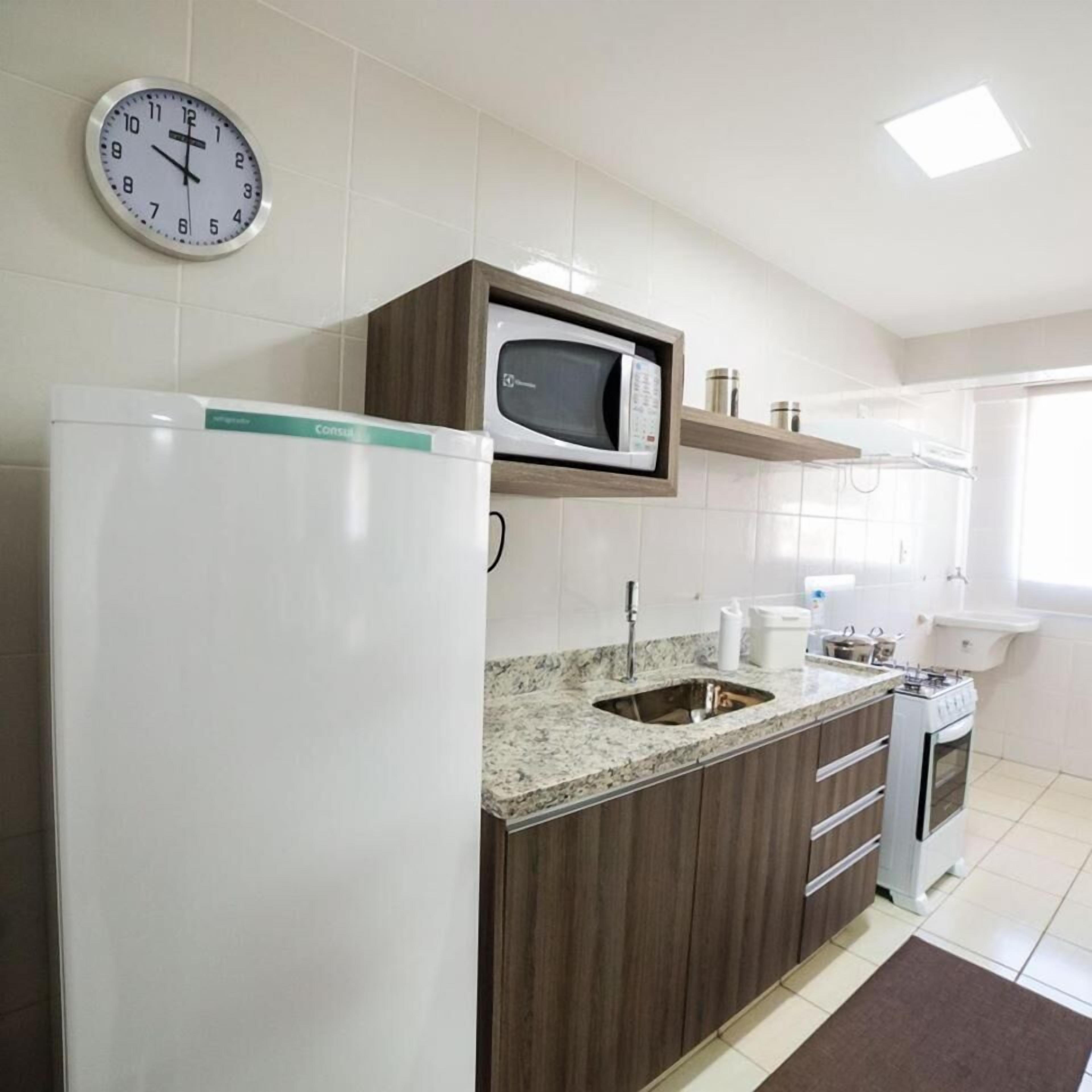 A kitchen with a refrigerator, microwave, sink, stove, and a clock on the wall.