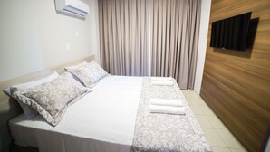 A hotel room with a bed, a flat-screen TV mounted on a wooden wall, and a window with curtains. - Serra Madre Residence (Rio Quente)