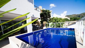 A swimming pool with blue tiles, surrounded by a white building and greenery. - Serra Madre Residence (Rio Quente)
